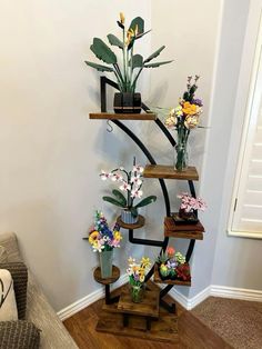 three wooden shelves with flowers and plants on them in the corner of a living room