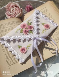 an open book with pink roses on it and ribbon tied around the edge, sitting on a table