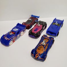 five toy cars are lined up on a white surface, one is blue and the other is red