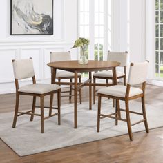 a dining table with four chairs and a vase on the floor in front of it