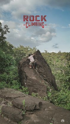 a man climbing up the side of a rock with trees and bushes in the background