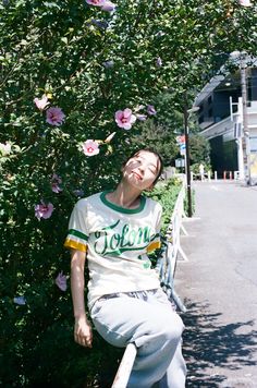 a man sitting on a bench next to a bush with pink flowers in the background