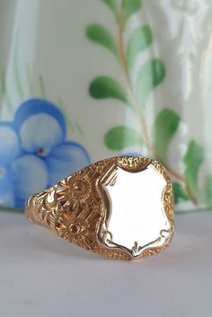 Glorious ornately engraved shoulders are the dream features of this solid gold vintage signet ring. The deeply engraved botanical designs along the shoulders create luxurious rich textures that contrast wonderfully against the simplicity of the shield and band.  The blank shield allows you to personalise the ring. Perhaps with your own initials, with initials of a loved one as a gift or memorial ring. Or, engraved with a date to celebrate a wedding or graduation. Personalising the ring will defi Luxury Gold Ring With Engraving Option, Luxury Yellow Signet Ring For Gift, Luxury Vintage Oxidized Signet Ring, Luxury Vintage Memorial Ring, Luxury Yellow Gold Memorial Ring, Classic Gold Engraved Ring For Ceremonial Use, Victorian Yellow Gold Etched Rings, Victorian Etched Yellow Gold Rings, Victorian Gold Engraved Etched Ring