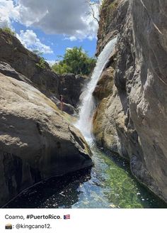 a man standing on the side of a waterfall next to a body of water with rocks surrounding it