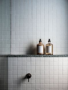 two soap dispensers sitting on top of a white tiled wall next to a black faucet