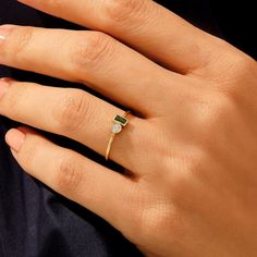 a woman's hand wearing a gold ring with an emerald stone in the middle