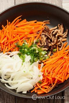 carrots, onions and mushrooms are being cooked in a skillet on a wooden table