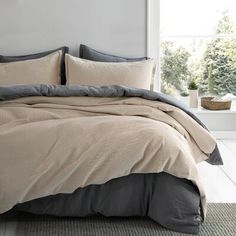 a bed with grey and beige comforters in a white room next to a window