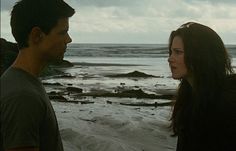 a man and woman standing on top of a sandy beach next to the ocean under a cloudy sky