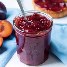 a glass jar filled with jam next to sliced peaches on a blue cloth and two pieces of bread in the background