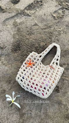 a crocheted bag sitting on top of a beach next to a small flower