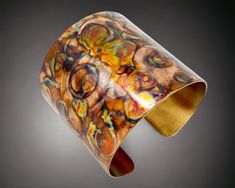 an artistic glass bracelet with gold and multicolored swirls on the outside, in front of a gray background