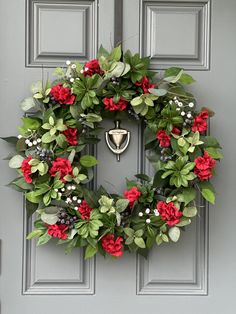 a wreath with red flowers and greenery hangs on the front door of a house