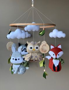 three stuffed animals hanging from a mobile in the shape of an owl, fox, and raccoon