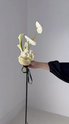 a hand holding a bouquet of flowers on top of a black stand with white walls in the background