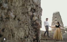 a man and woman standing on some steps holding each other's hands in front of an old building