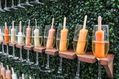 Champagne glasses filled with colorful popsicles are displayed from shelves on a boxwood greenery wall. Mimosa Bar Wedding Reception, Treat Wall Party, Wedding Drink Display, Unique Mimosas, Wall Styling Ideas, Mimosa Bar Set Up, Champagne Bar Ideas, Champagne Party Decorations, Champagne Wall Ideas