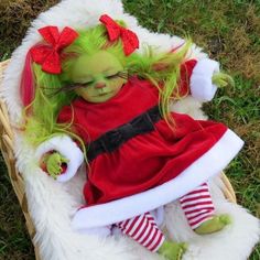 a doll with green hair wearing a red dress and santa claus hat sitting in a basket