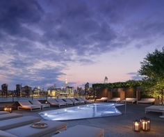 an outdoor swimming pool surrounded by lounge chairs and trees with the city skyline in the background