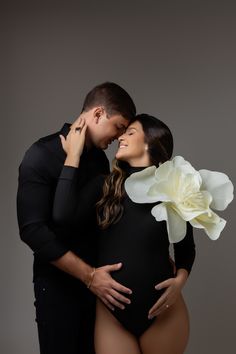 a pregnant woman is hugging her husband's belly with a flower on his chest