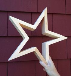 a hand holding a wooden star in front of a red building