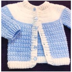 a blue and white crocheted cardigan with buttons on the front, sitting on a black surface