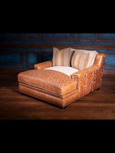 a brown leather chair with pillows on it sitting in front of a blue wall and wooden floor