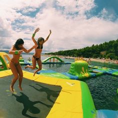 two girls jumping on a bouncy course in the water