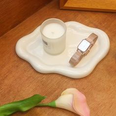 a candle, watch and flower on a white tray with a pink rose next to it