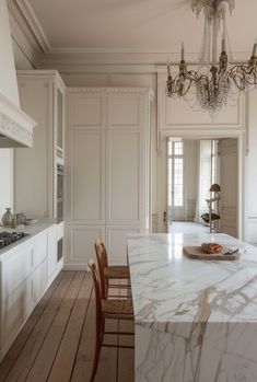 an elegant kitchen with marble counter tops and white cabinets, chandelier above the island