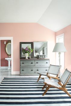 a living room with pink walls and striped rug on the floor, two chairs in front of a dresser