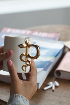 a person holding a coffee cup with a gold caduce on the top and an open book in the background