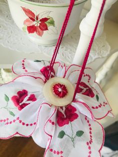 a red and white flower is hanging from a table with a cup in the background