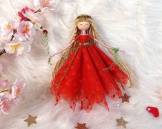 a doll with long blonde hair wearing a red dress sitting on a white fur background