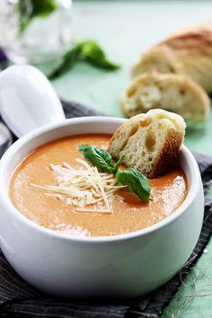 a bowl of tomato soup with bread and parmesan cheese on the side, ready to be eaten