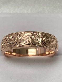 a gold wedding ring with an intricate design on the front and side, sitting on a white surface