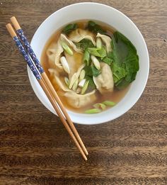 two chopsticks sit next to a bowl of soup with dumplings and spinach