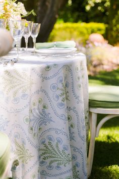 the table is set for two outside in the grass with flowers and glasses on it