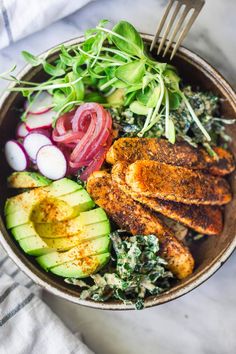 a bowl filled with chicken, spinach and sliced avocado next to a fork