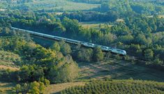 an aerial view of a train traveling through the country side with trees in the foreground