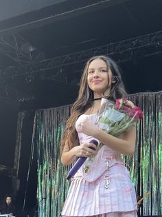 a girl in a pink dress holding flowers and a purple umbrella at an outdoor concert