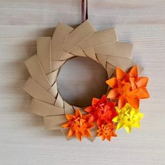 an origami wreath made out of brown paper with orange, yellow and red flowers