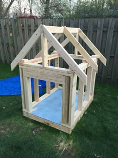 a house made out of wood sitting on top of green grass next to a blue tarp