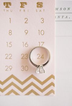 a wedding ring sitting on top of a white and gold calendar with the date in it