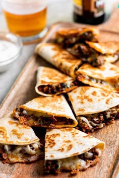 several quesadillas cut in half on a cutting board next to a glass of beer