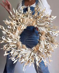 a woman wearing overalls and holding a wreath made out of dried grass with white flowers