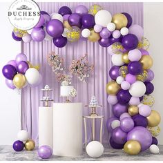 a purple and gold balloon arch with white vases, cake and flowers on it