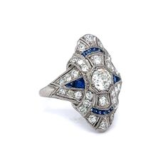 This eye-catching Art Deco ring features 1.68 carats of diamonds and .40 carats of blue sapphires in shimmering platinum. A single .60 carat Old European cut diamond decorates the center of the ring. Four (4) .06 carat accent diamonds are mounted down the center of the ring. An additional twenty-eight (28) single cut diamonds form a unique cluster design on the elegant mounting. The French cut blue sapphires fill the spaces of the diamond mountings, bringing a royal blue depth of color to the mi