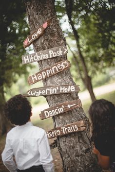 a man and woman standing next to a tree with wooden signs attached to it's trunk