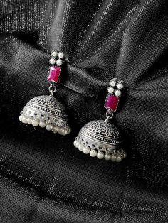 two silver bells with red stones hanging from the end of each earring, on a black fabric background